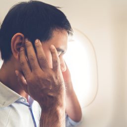 Man on airplane experiencing ear troubles.
