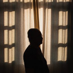 A silhouette of a person standing close to a window indoors.