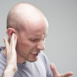 Man suffering from hearing loss holding his ear.